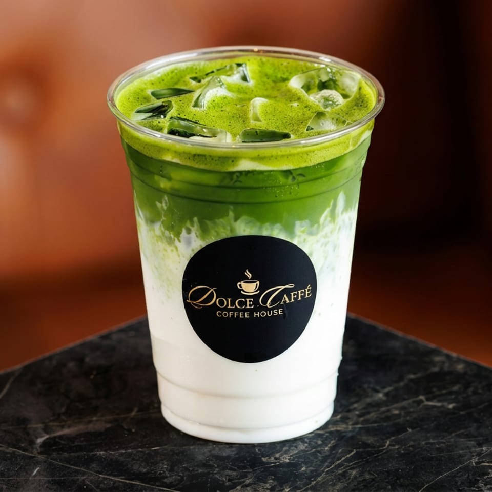 Iced green matcha latte in a branded Dolce Caffè Coffee House cup on a black marble table.